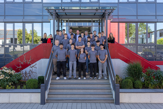 22 neue Auzsubildende stehen auf der Treppe vor dem Kassecker-Veraltungsgebäude in Waldsassen; Sie tragen graue Kassecker-Shirts. Mit ihnen im Bild stehen die Kassecker-Geschäftsführer.