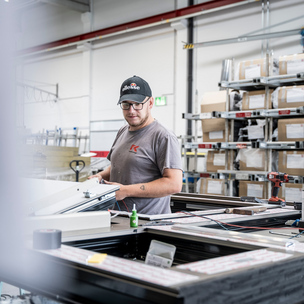 Mitarbeiter des Kassecker Stahl- und Metallbaus Junger Mann steht in einer Produktionshalle an einem Fensterrahmen und montiert.